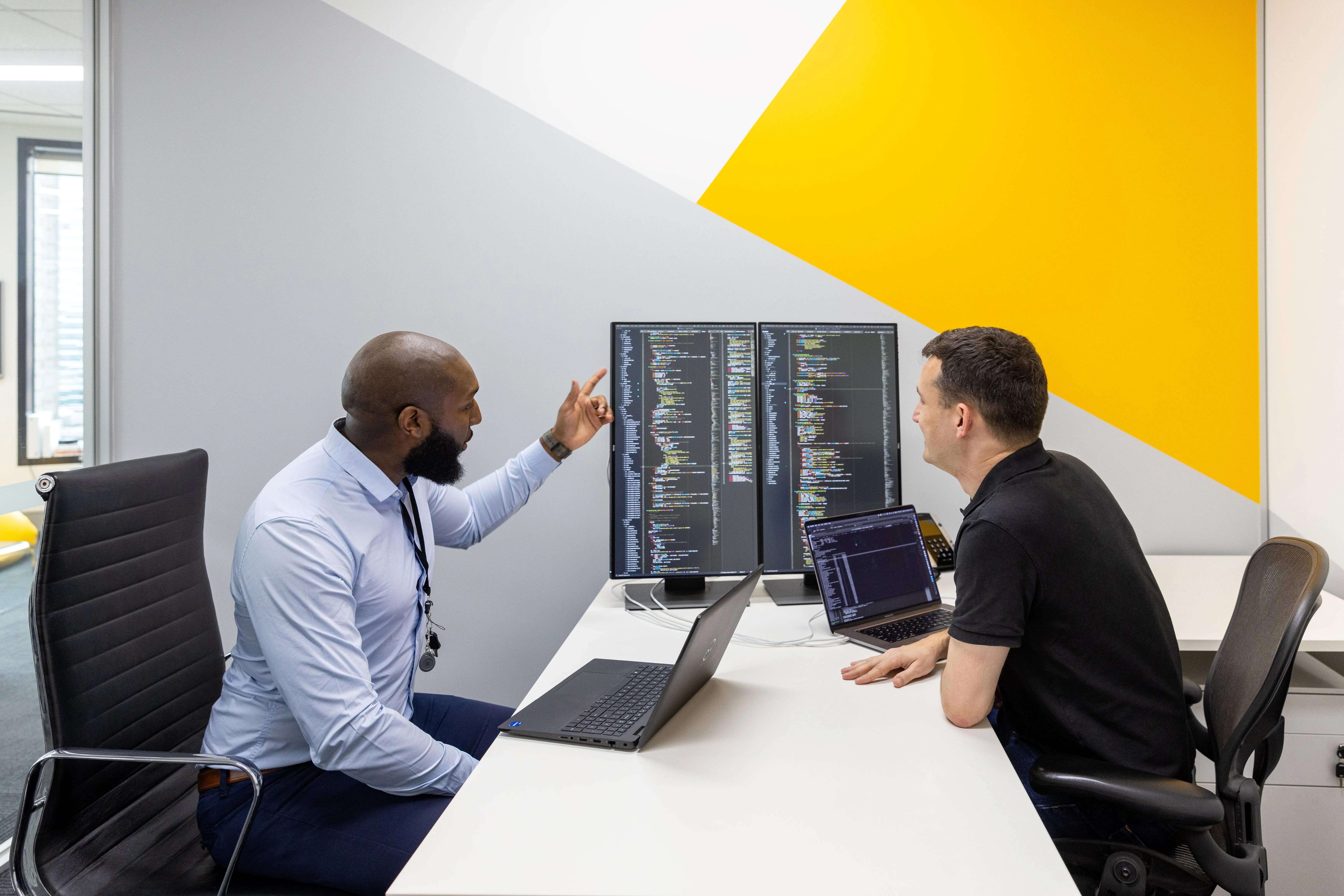 2 men looking at code on large screen